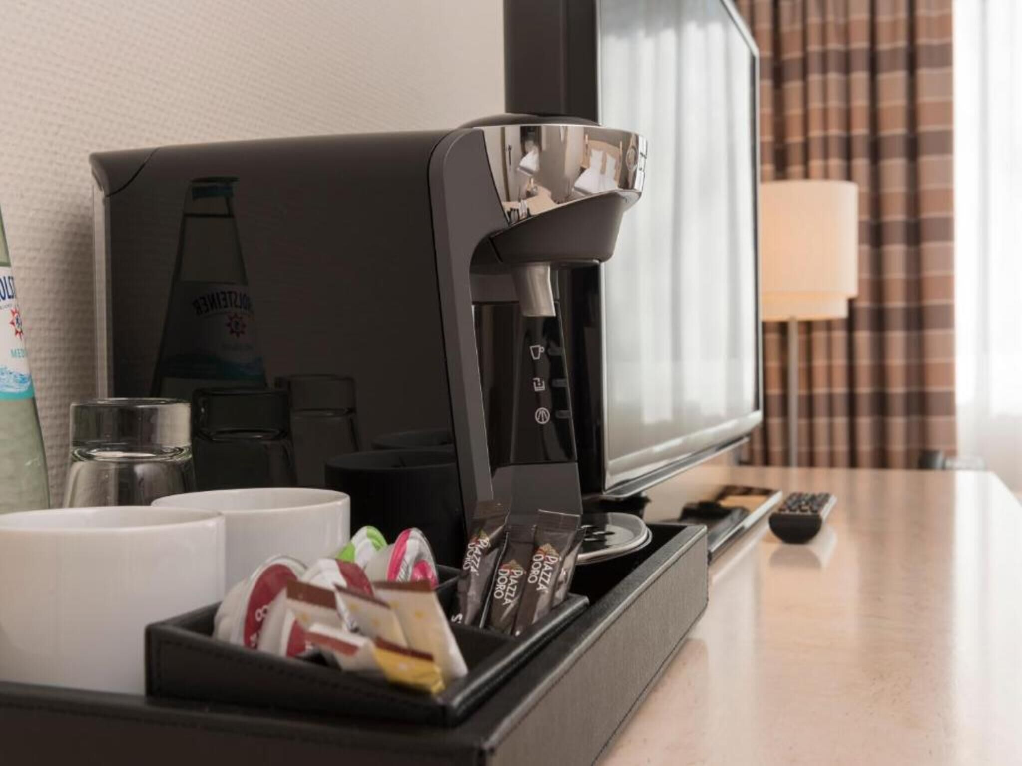 A hotel room with a coffee machine, a television, and a tray with snacks.