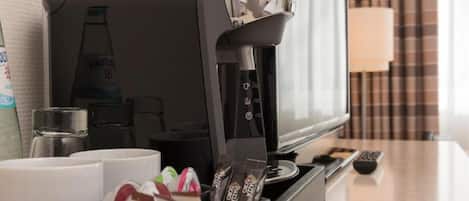 A hotel room with a coffee machine, a television, and a tray with snacks.