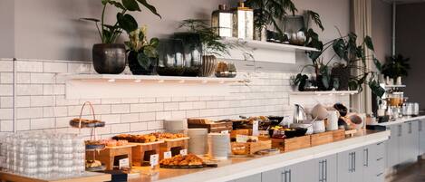 A buffet with various food items and a white tiled backsplash with plants.