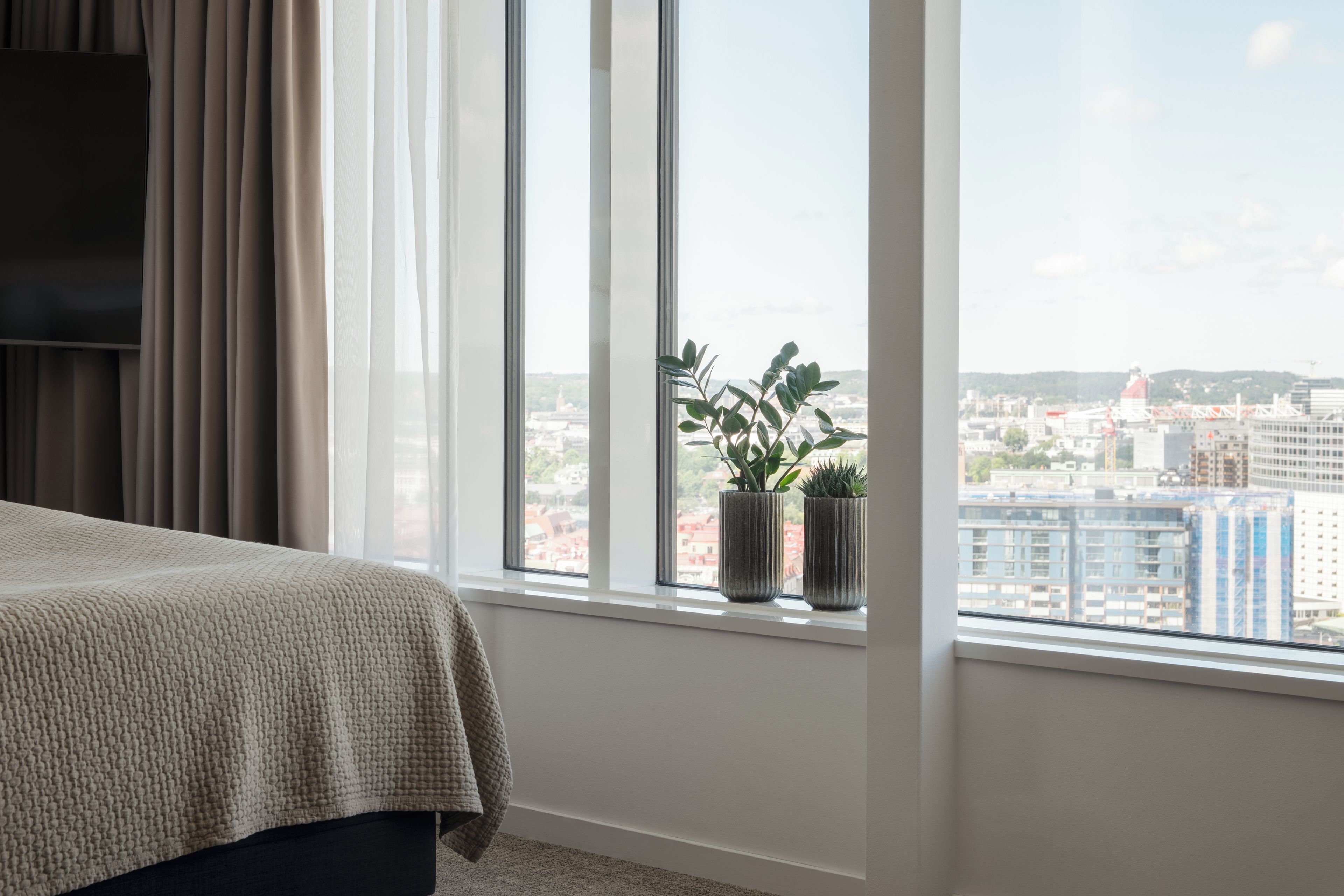 A bedroom with a large window, a bed, and two potted plants.