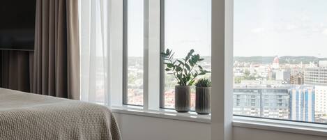 A bedroom with a large window, a bed, and two potted plants.