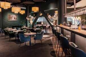Un área de bar moderna con mesas redondas, taburetes y lámparas colgantes.