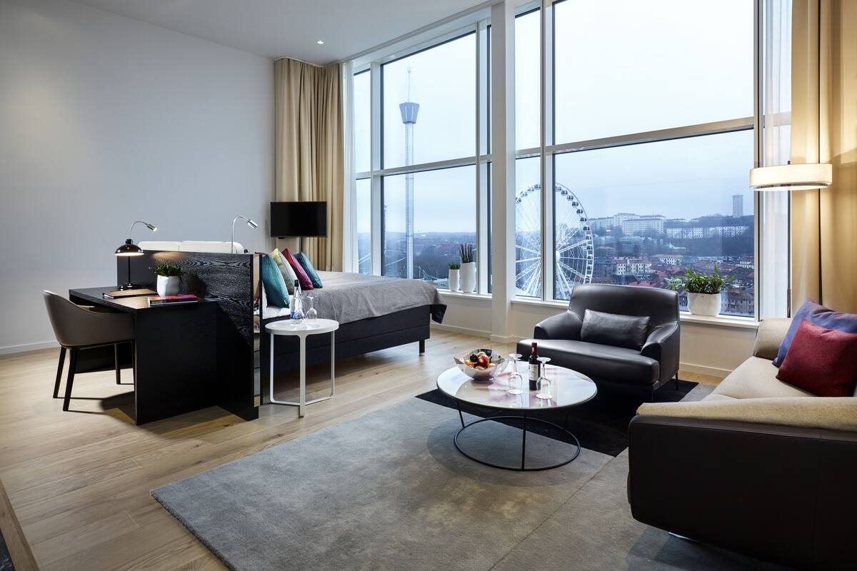 Ein modernes Hotelzimmer mit einem großen Bett, einem Schreibtisch, einer Sitzecke und Blick auf ein Riesenrad.