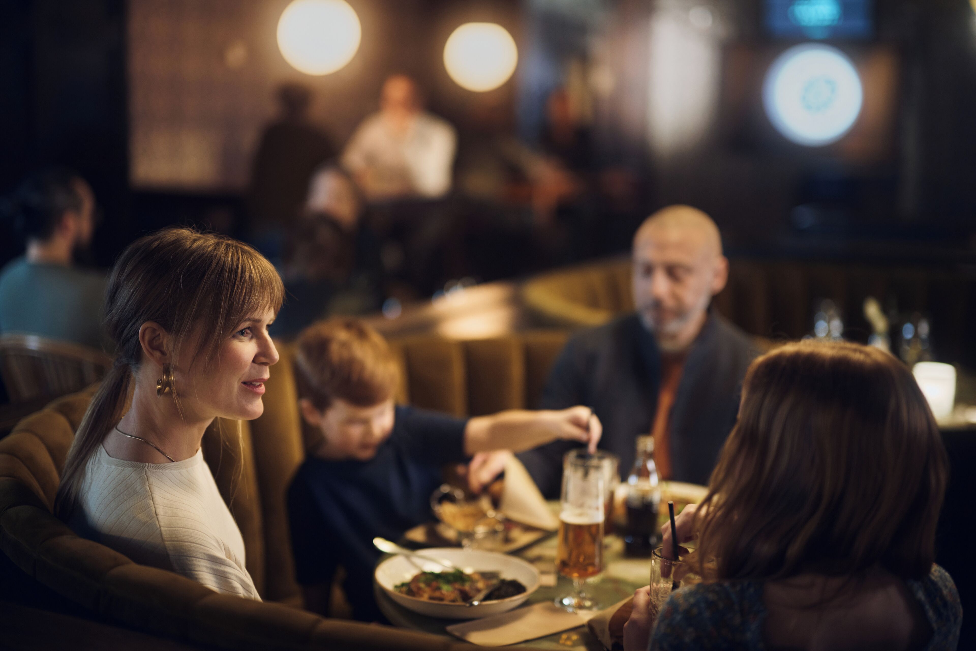A restaurant interior with diners seated at tables, a bar area in the background, and a casual dining atmosphere.