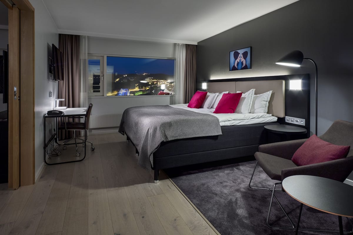Ein modernes Hotelzimmer mit einem großen Bett, einem Schreibtisch und Blick auf die nächtliche Stadt.