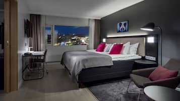 Ett modernt hotellrum med en stor säng, ett skrivbord och utsikt över staden på natten.