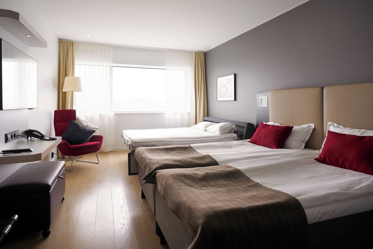 Ein Hotelzimmer mit zwei Betten, einem Schreibtisch, einem Stuhl und einem großen Fenster mit Vorhängen.