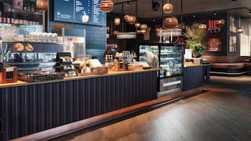 Zona de bar moderna con una pantalla de menú, varias botellas de bebidas y un área de estar con una planta.