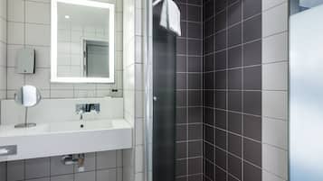 A modern bathroom with a white sink, a round mirror, and a glass-enclosed shower.