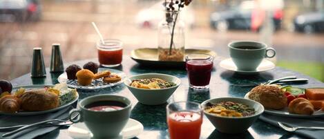 Una mesa de desayuno con diversos alimentos y bebidas, como pasteles, frutas y refrescos.