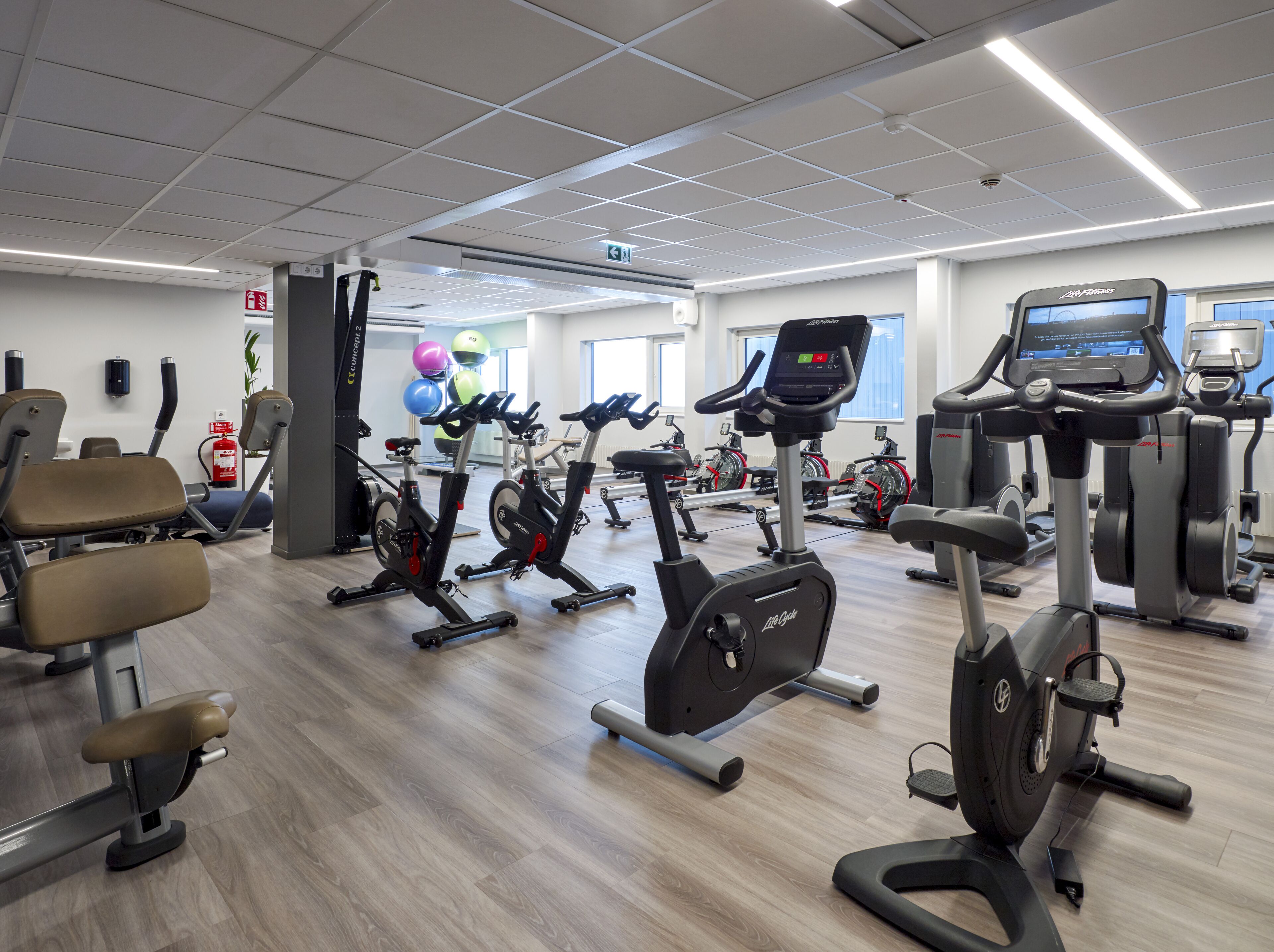 A gym with various exercise machines, a fire extinguisher, and a water dispenser on the wall.