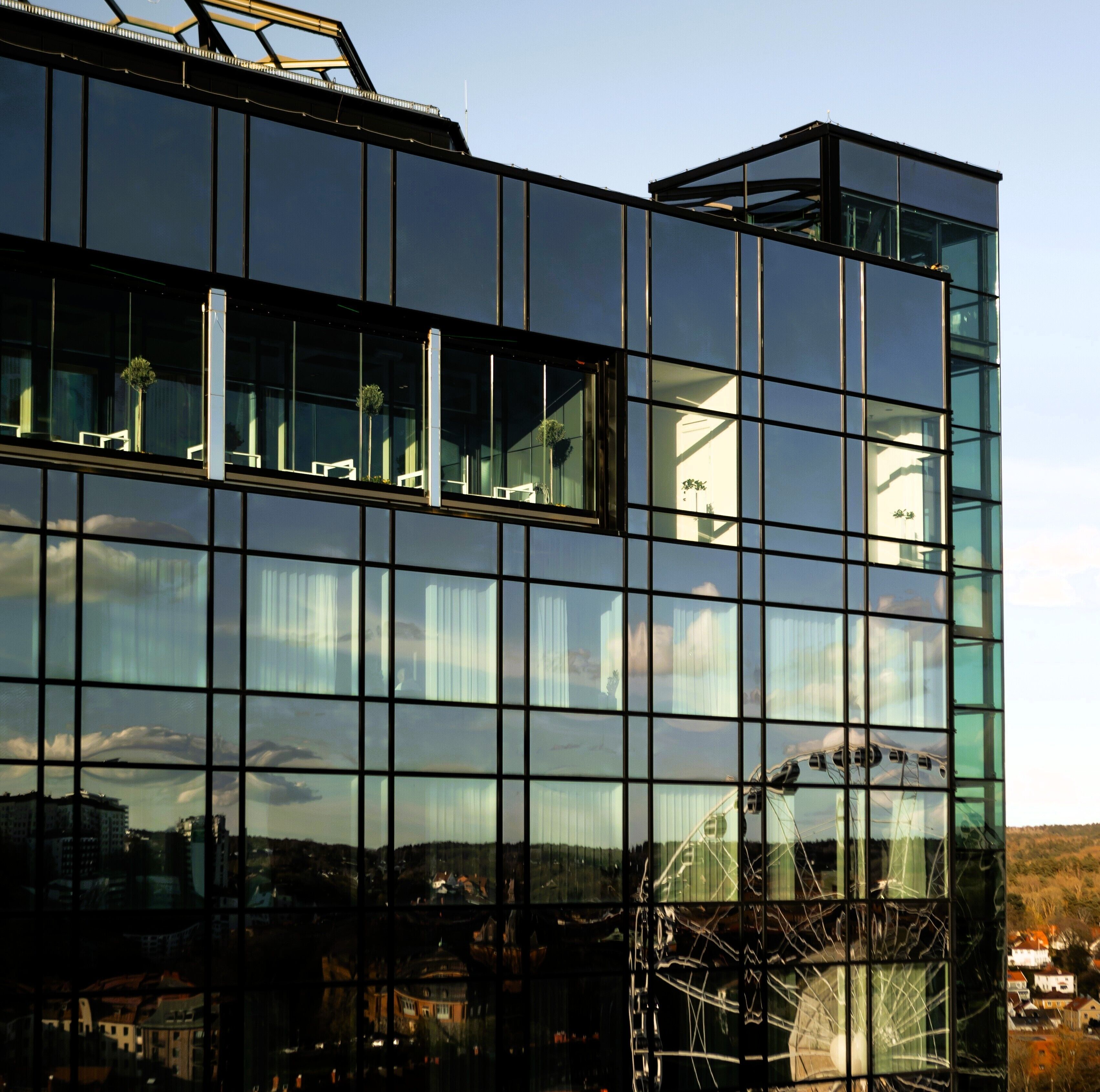 En modern byggnad med stora glasfönster som speglar himlen och de omgivande byggnaderna.
