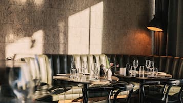 A restaurant with leather booths, round tables, and a stone wall.