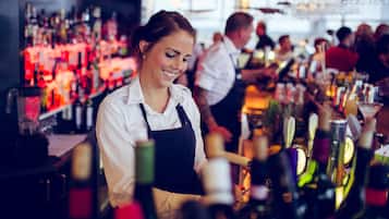 A bar with shelves of bottles and glasses, a bartender in uniform, and patrons in the background.
