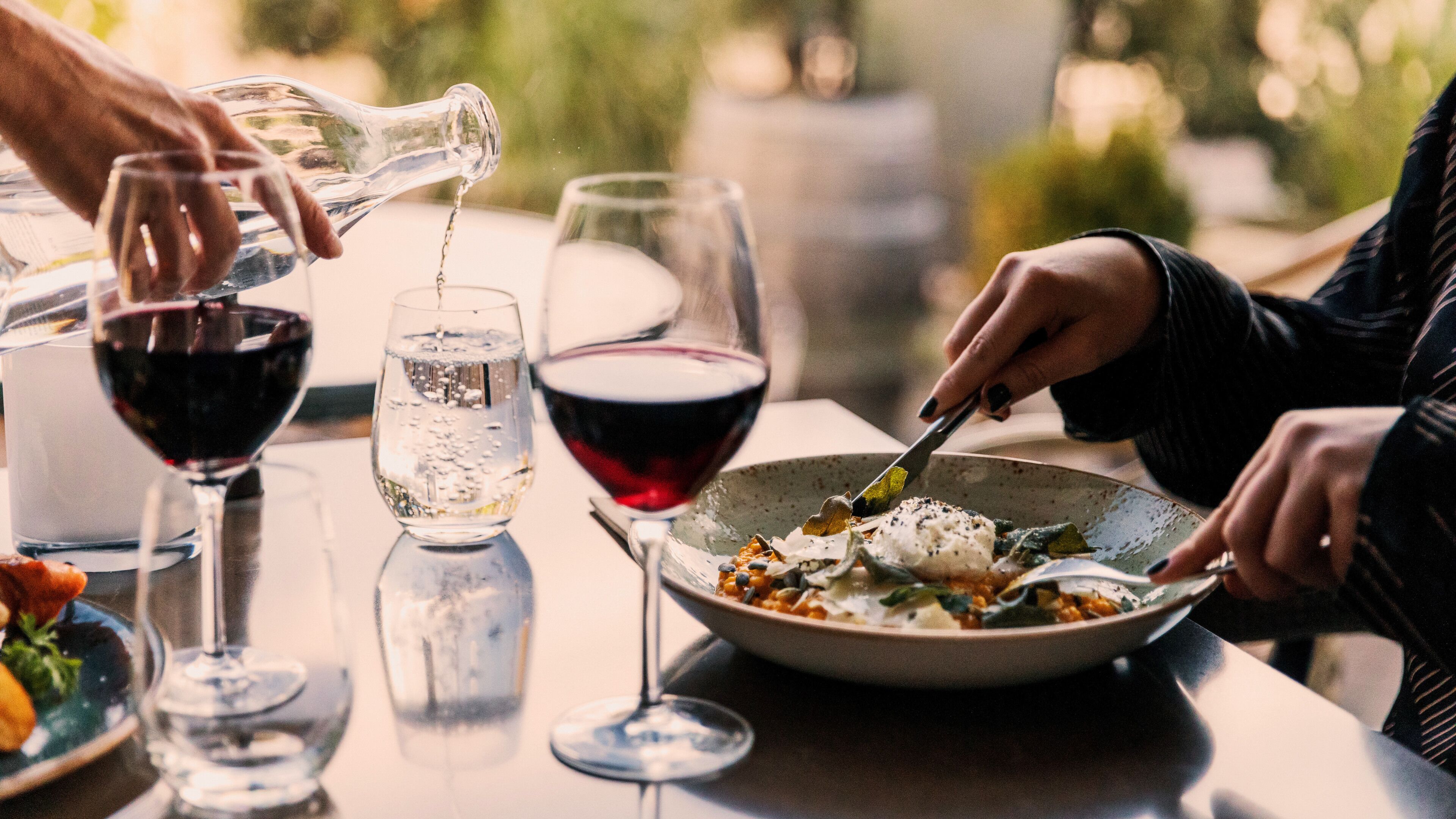 A dining table with a bowl of food, two glasses of wine, and a bottle being poured.