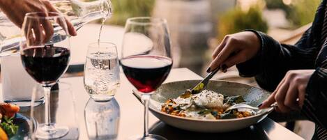 A dining table with a bowl of food, two glasses of wine, and a bottle being poured.