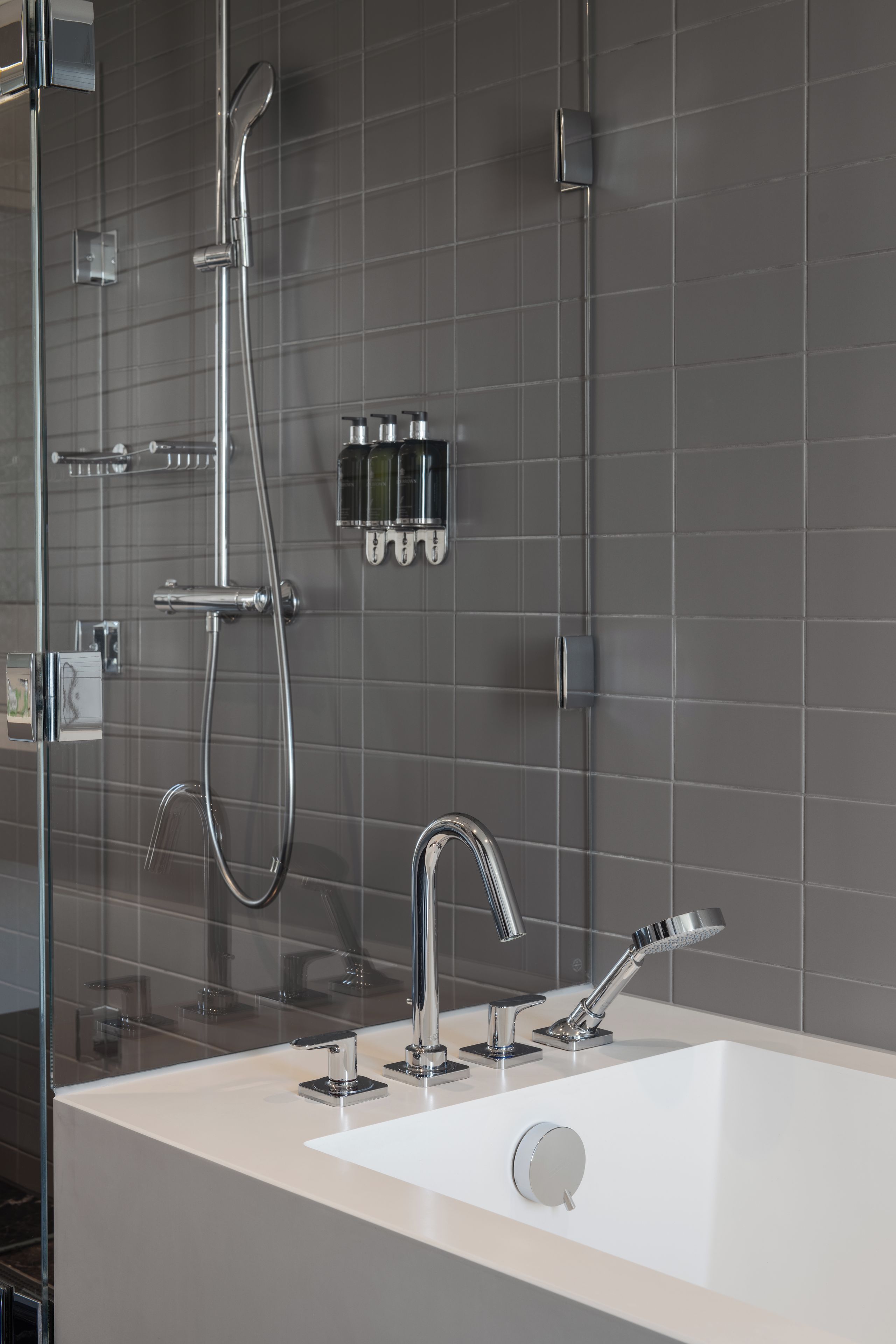 Un baño moderno con cabina de ducha de vidrio, un lavabo blanco e instalaciones cromadas.