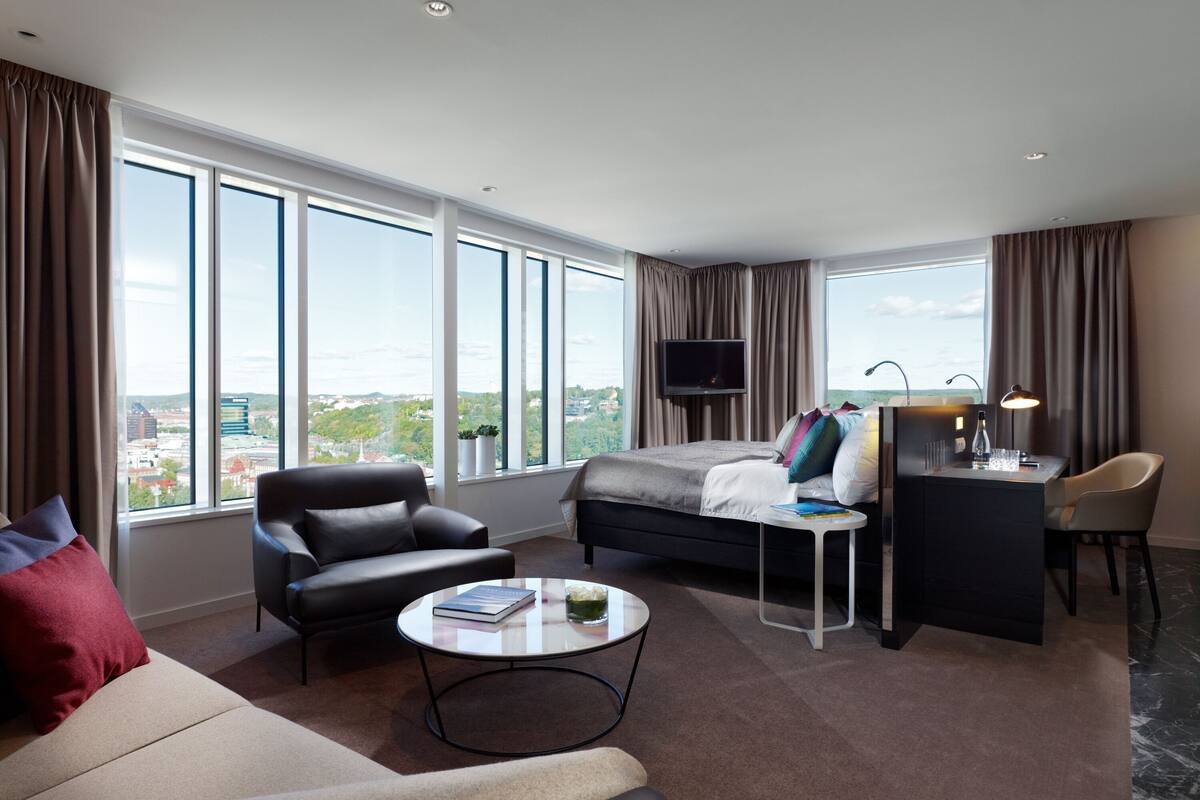 Ein modernes Hotelzimmer mit einem großen Bett, einem Schreibtisch, einem Sessel, einer Couch und einem Fernseher.