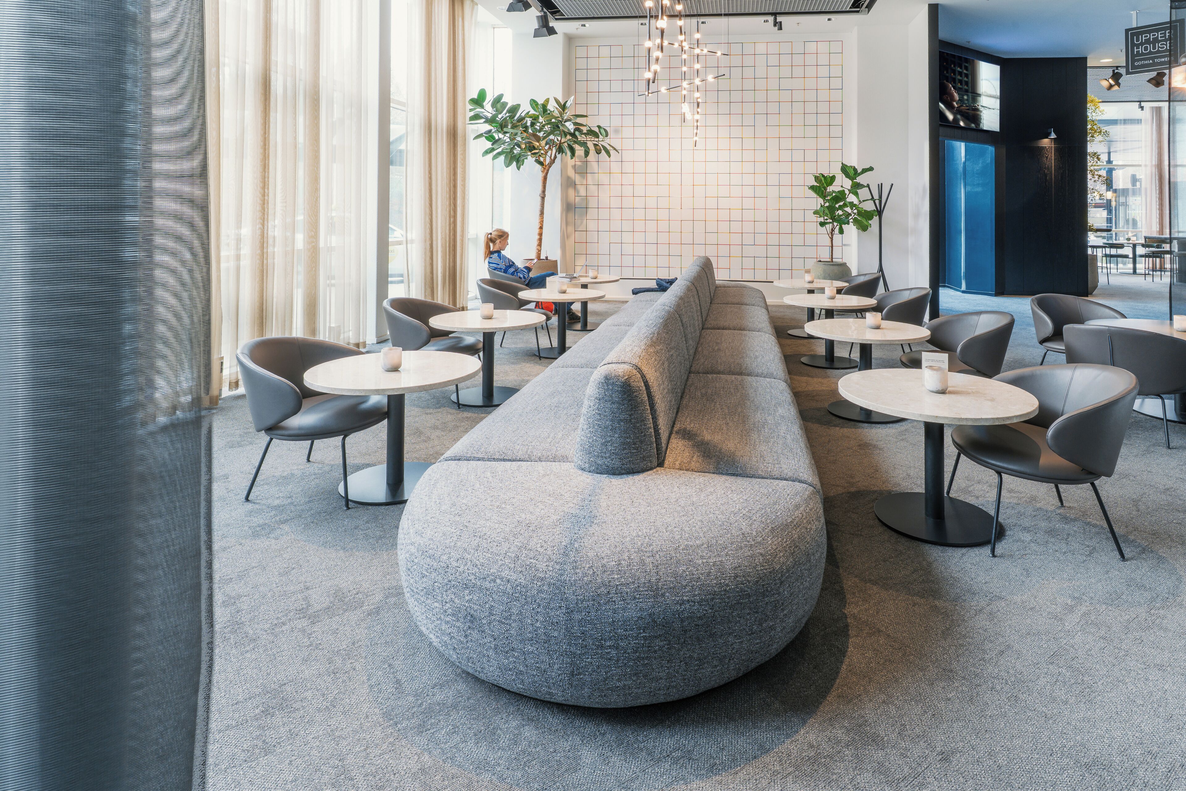 A modern lounge area with a long grey sofa, round tables, and chairs.
