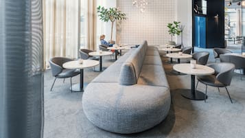A modern lounge area with a long grey sofa, round tables, and chairs.