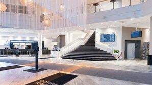Un hall d’hôtel moderne comprenant un comptoir d’accueil, un escalier et un écran numérique.