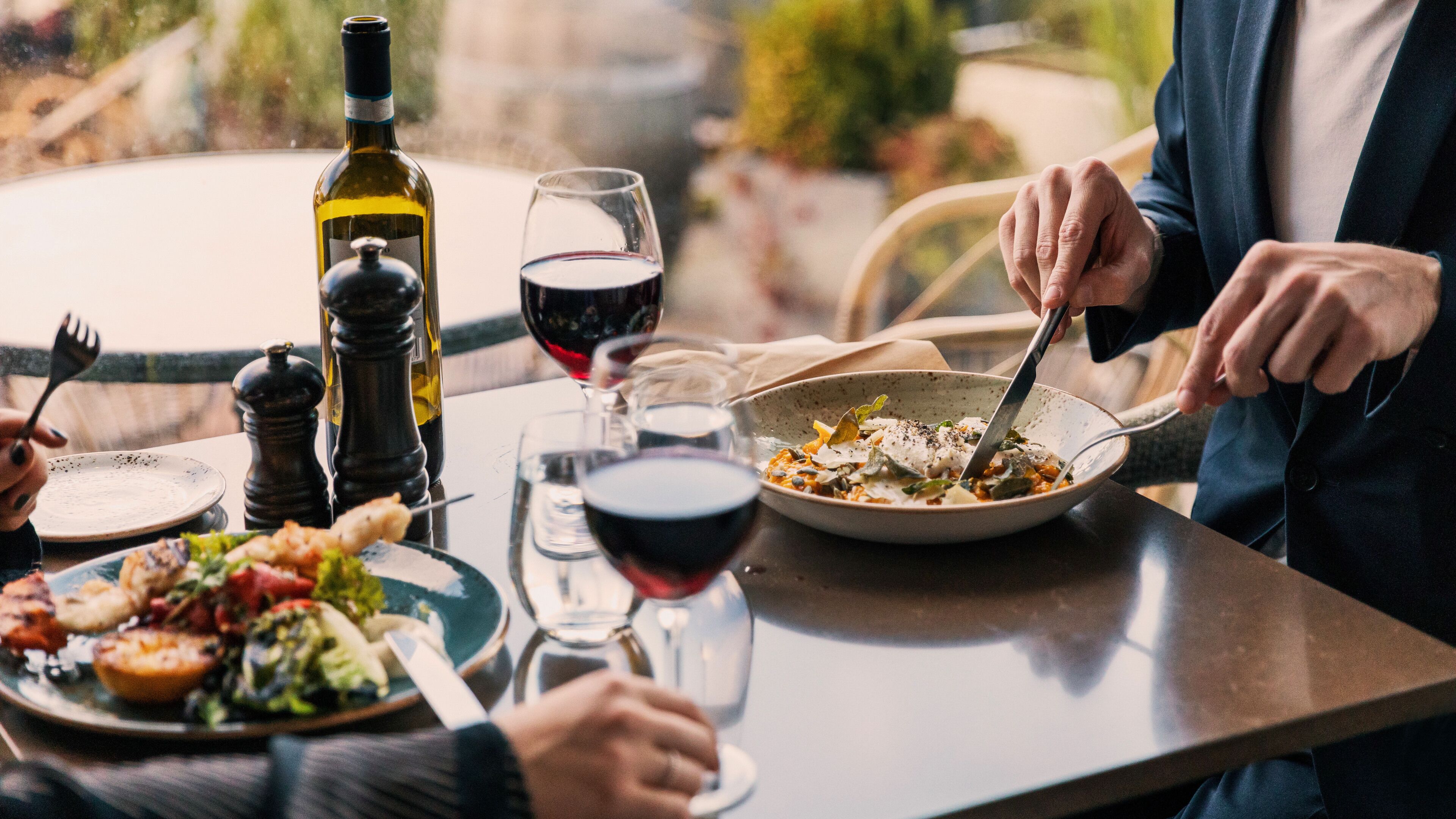 Una mesa de comedor con platos de comida, copas de vino y una botella de vino.
