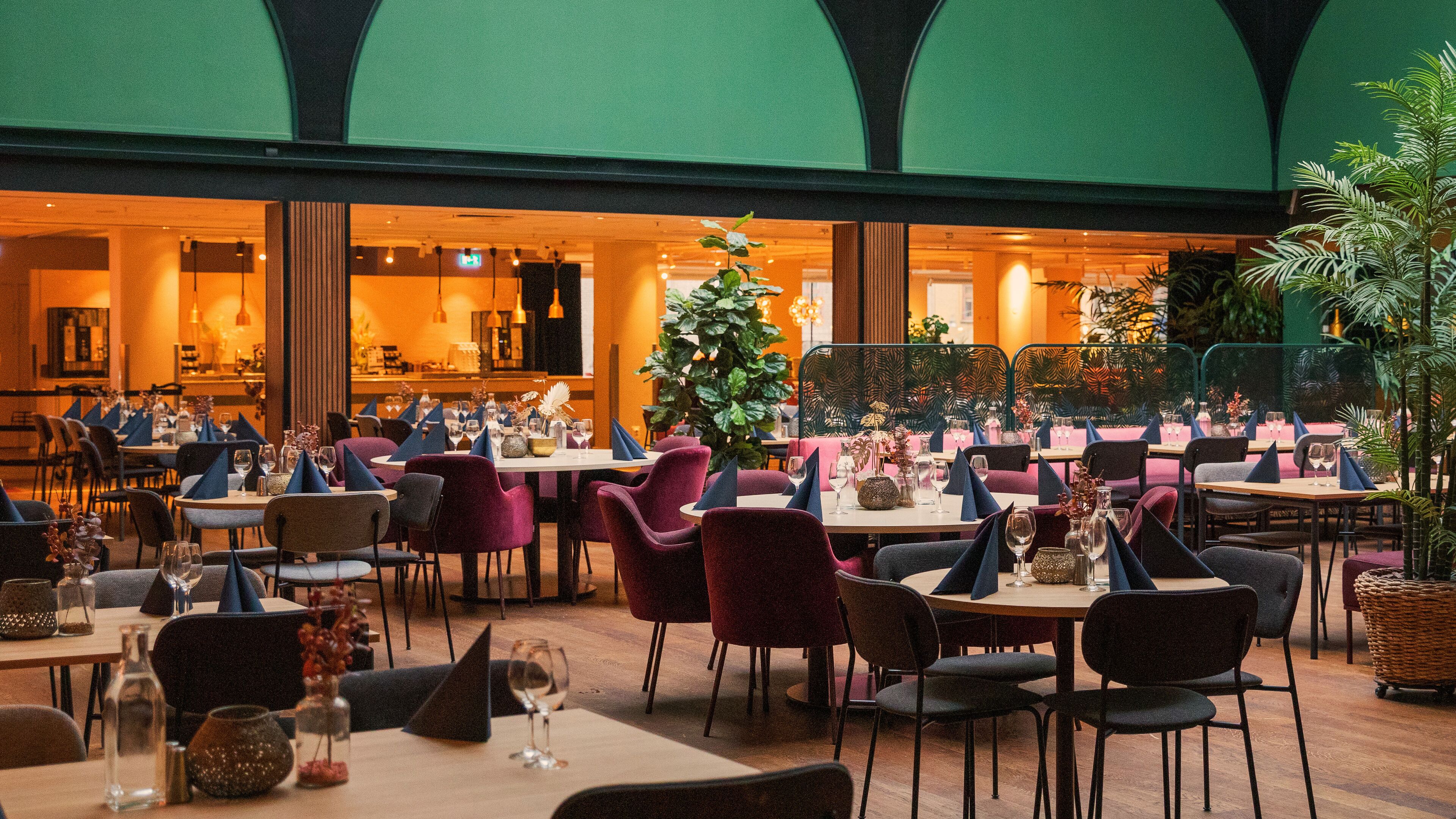 A restaurant with tables set for dining, chairs, and a large green plant in the center.