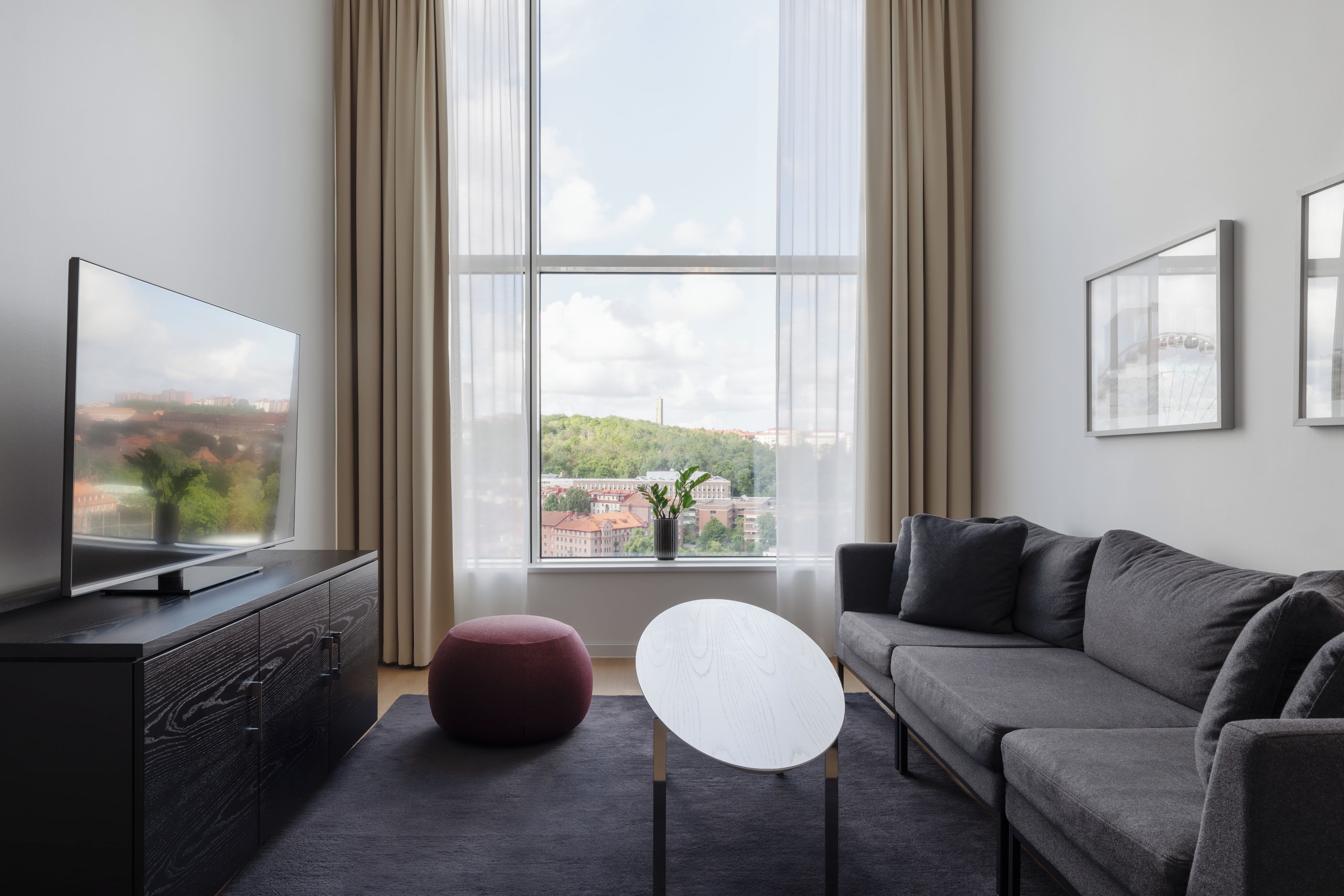 Un salon moderne doté d’un téléviseur à écran plat, d’un canapé gris, d’une table basse ronde et d’une grande fenêtre avec des rideaux.