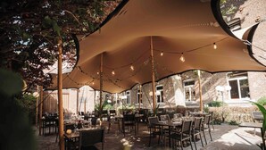 An outdoor patio area with tables and chairs under large umbrellas, surrounded by brick walls and greenery. - Blooma Hotel Liege Centre - Handwritten Collection (Liege)