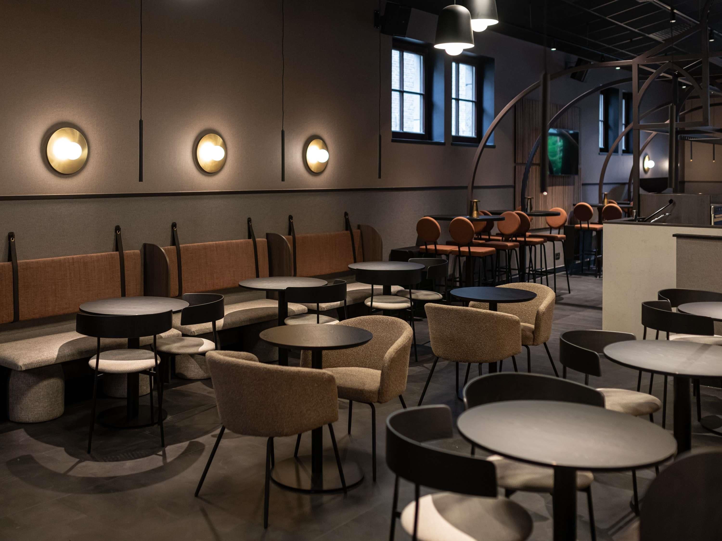 Un interior de restaurante moderno con mesas redondas, asientos acolchados e iluminación colgante.