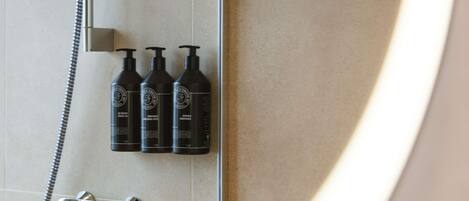A bathroom with a shower, a handheld showerhead, and three bottles of shampoo.