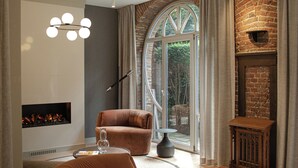 A modern living room with a fireplace, a large window, and a cozy seating area. - Blooma Hotel Liege Centre - Handwritten Collection (Liege)