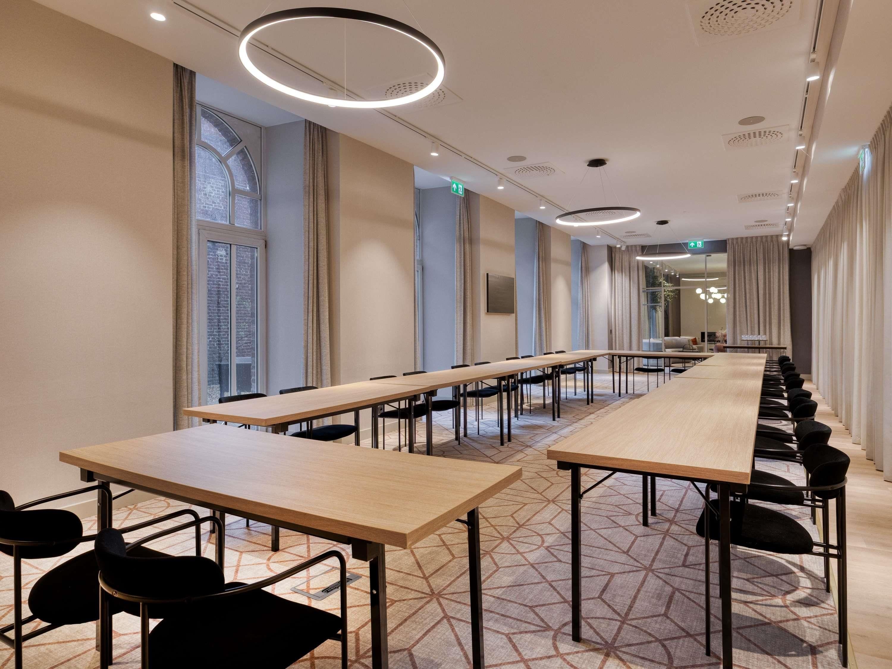 A conference room with long tables and chairs, large windows, and modern lighting fixtures.