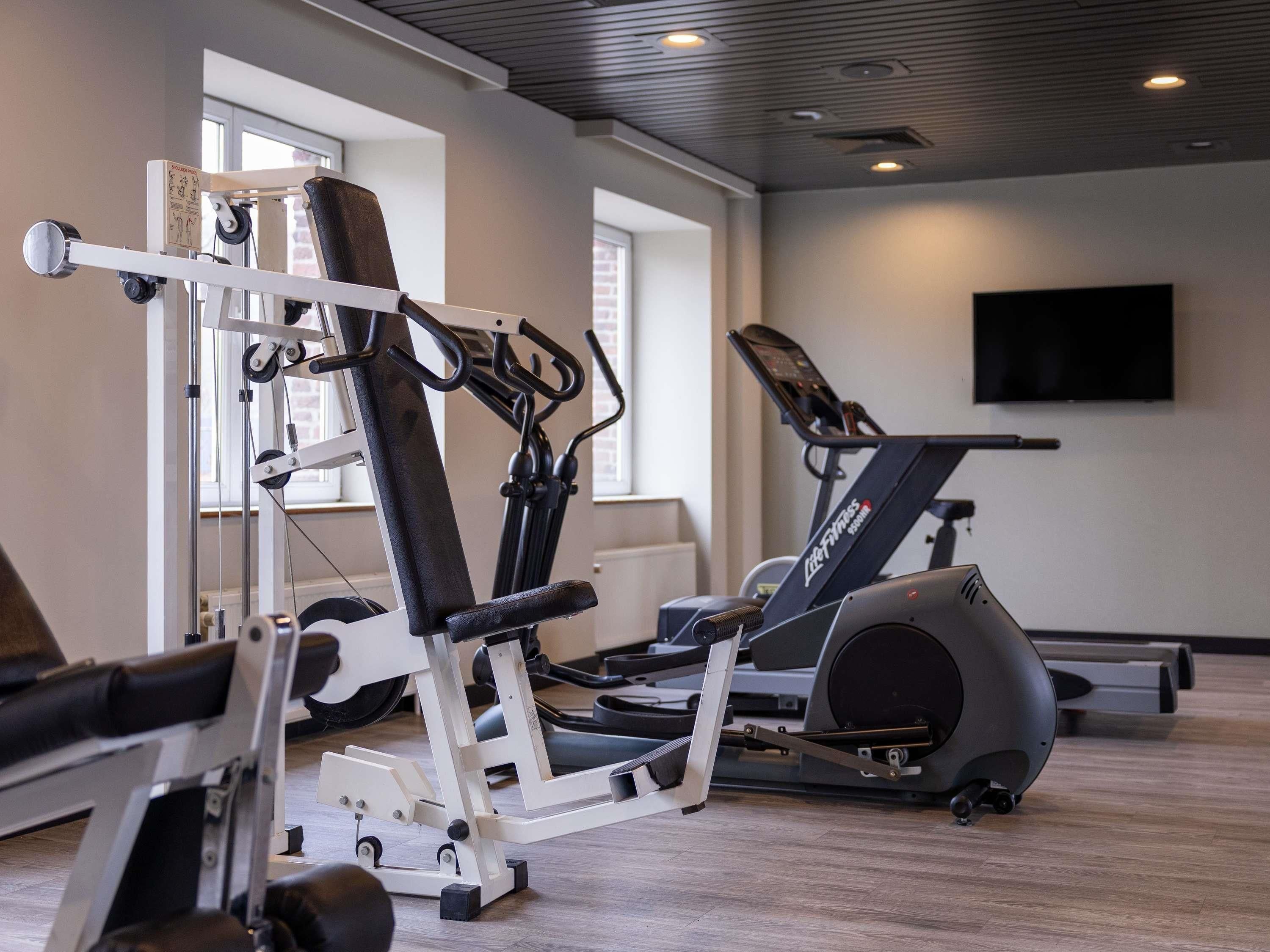 Un gimnasio con equipo de ejercicio, una cinta de correr y un televisor en la pared.