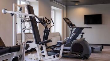 Uma academia com equipamento de exercícios, esteira e televisão na parede.