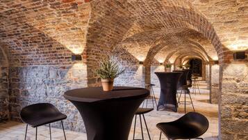 Un interior con arcos de piedra, una mesa redonda con una planta en maceta y sillas negras modernas.