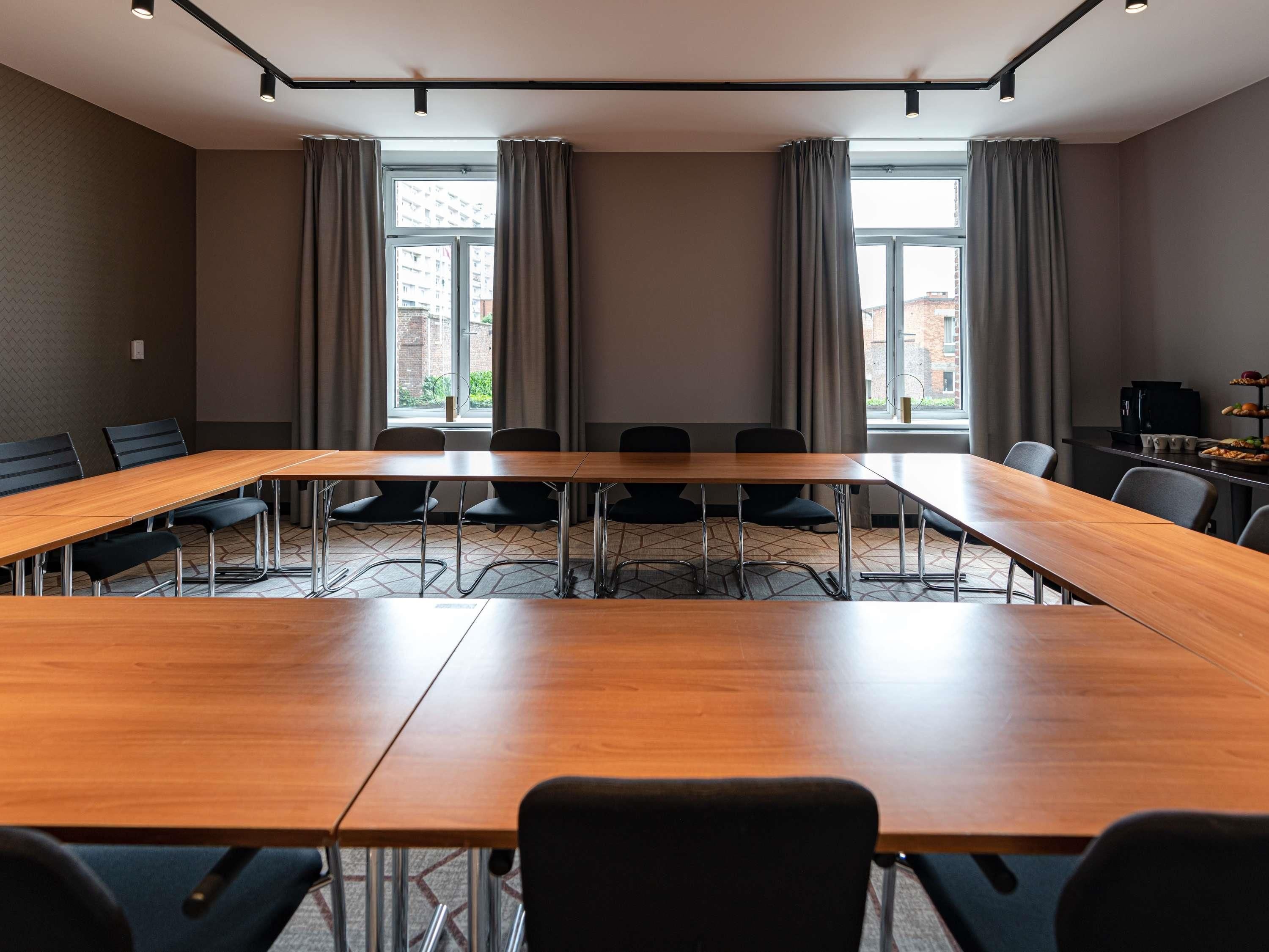 Un salón de conferencias con una larga mesa, sillas y ventanas amplias con cortinas.