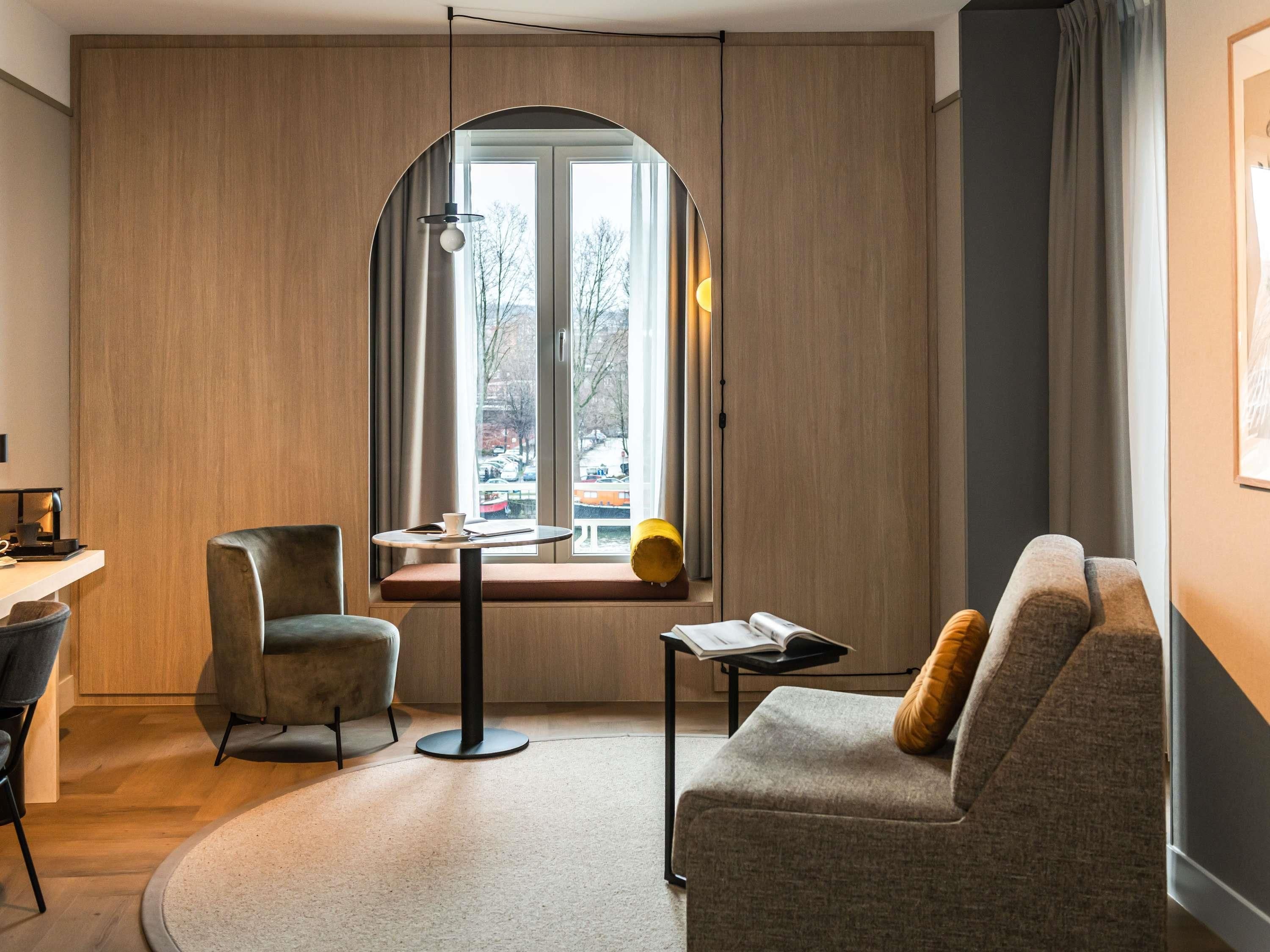 Une pièce moderne avec une fenêtre incurvée, une table ronde, un canapé et un fauteuil.