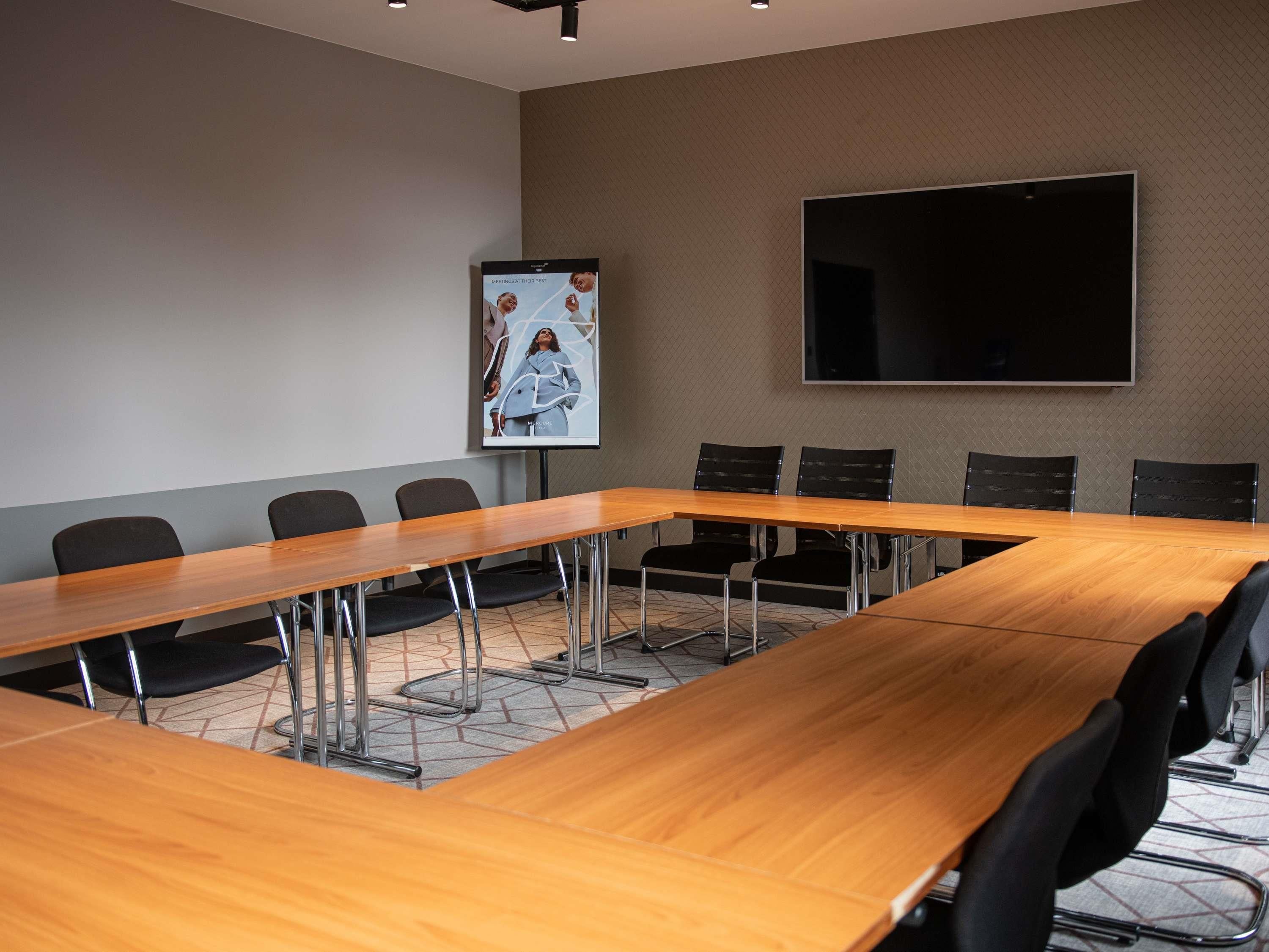 Un salón de conferencias con una larga mesa de madera, sillas negras, un televisor de pantalla plana grande y un cartel en la pared.