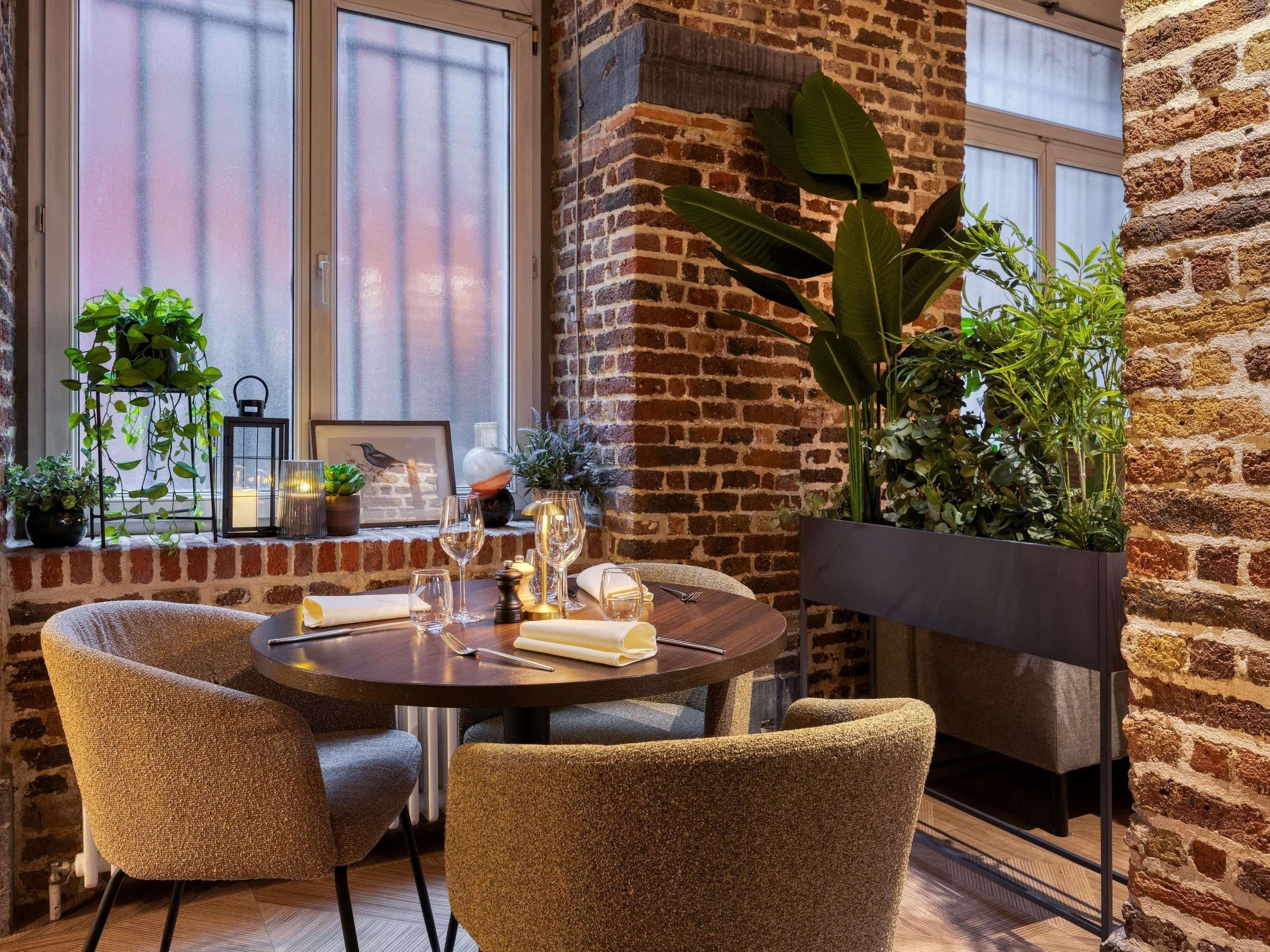 Un coin repas accueillant avec un mur en briques, une table ronde et des chaises, agrémenté de plantes en pot et d’un tableau encadré.