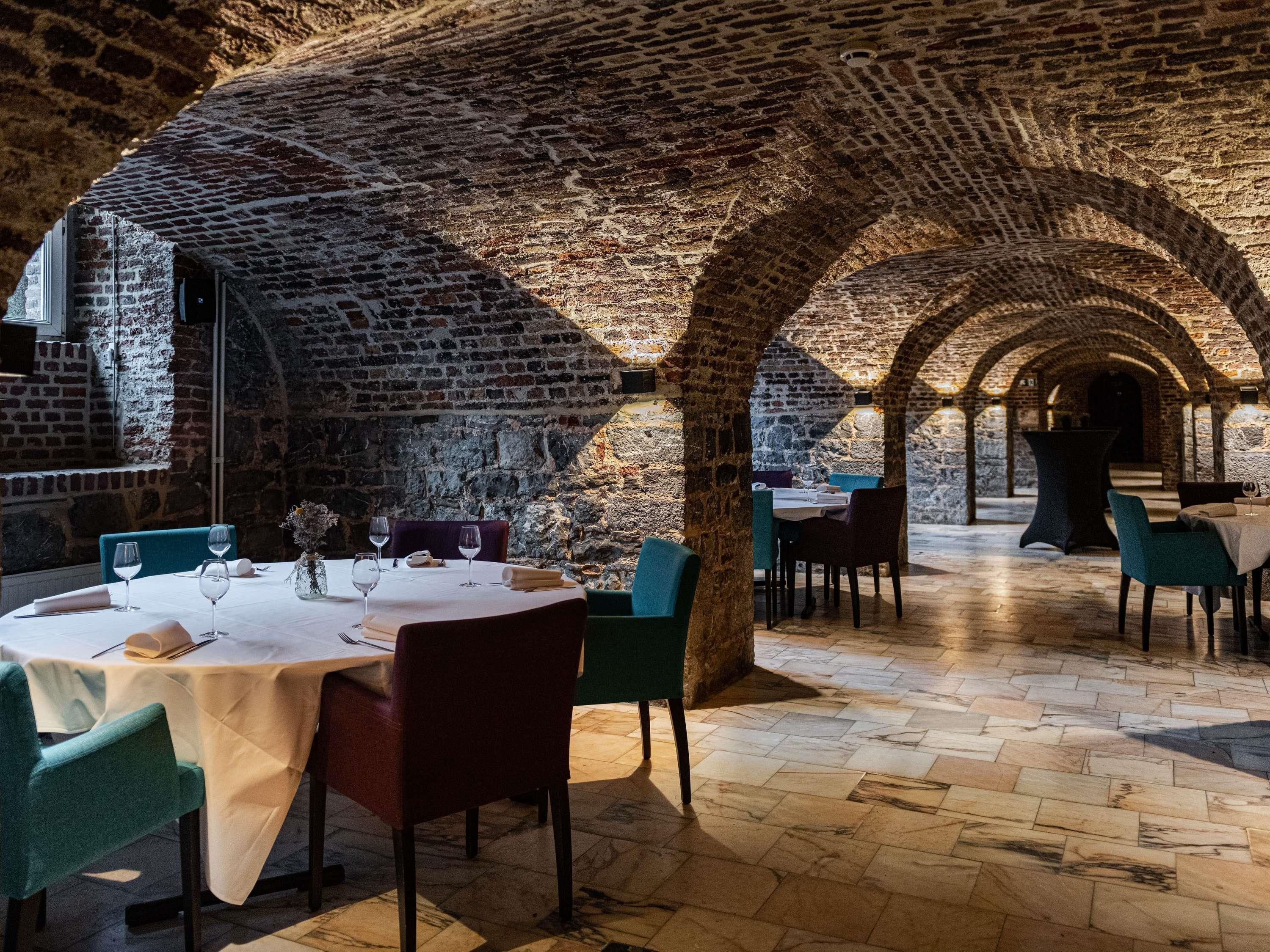 Een restaurant met bakstenen bogen, tafels met witte tafelkleden en stoelen.