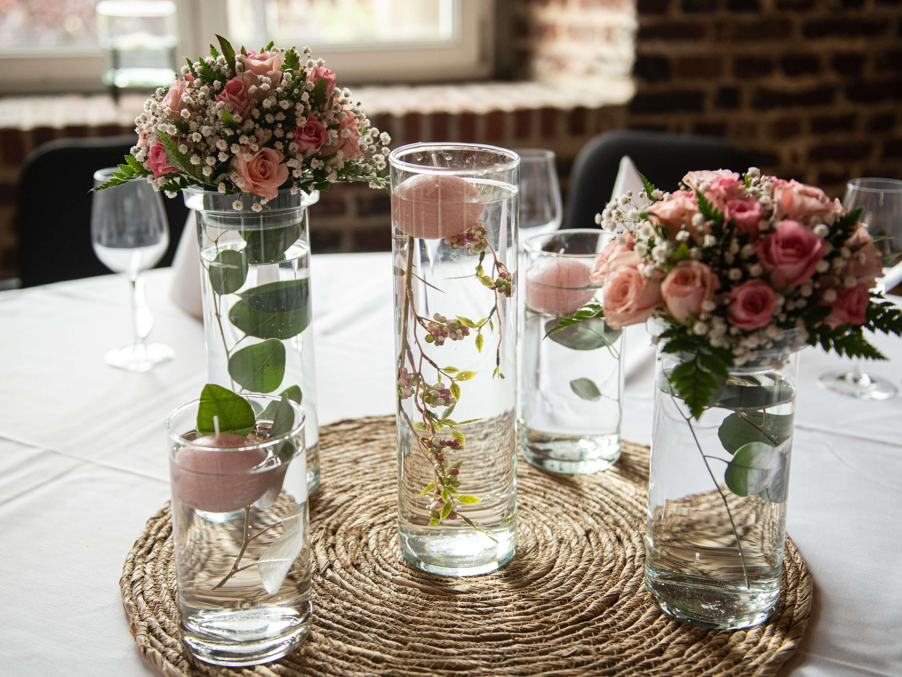 Three vases with flowers and water on a table.