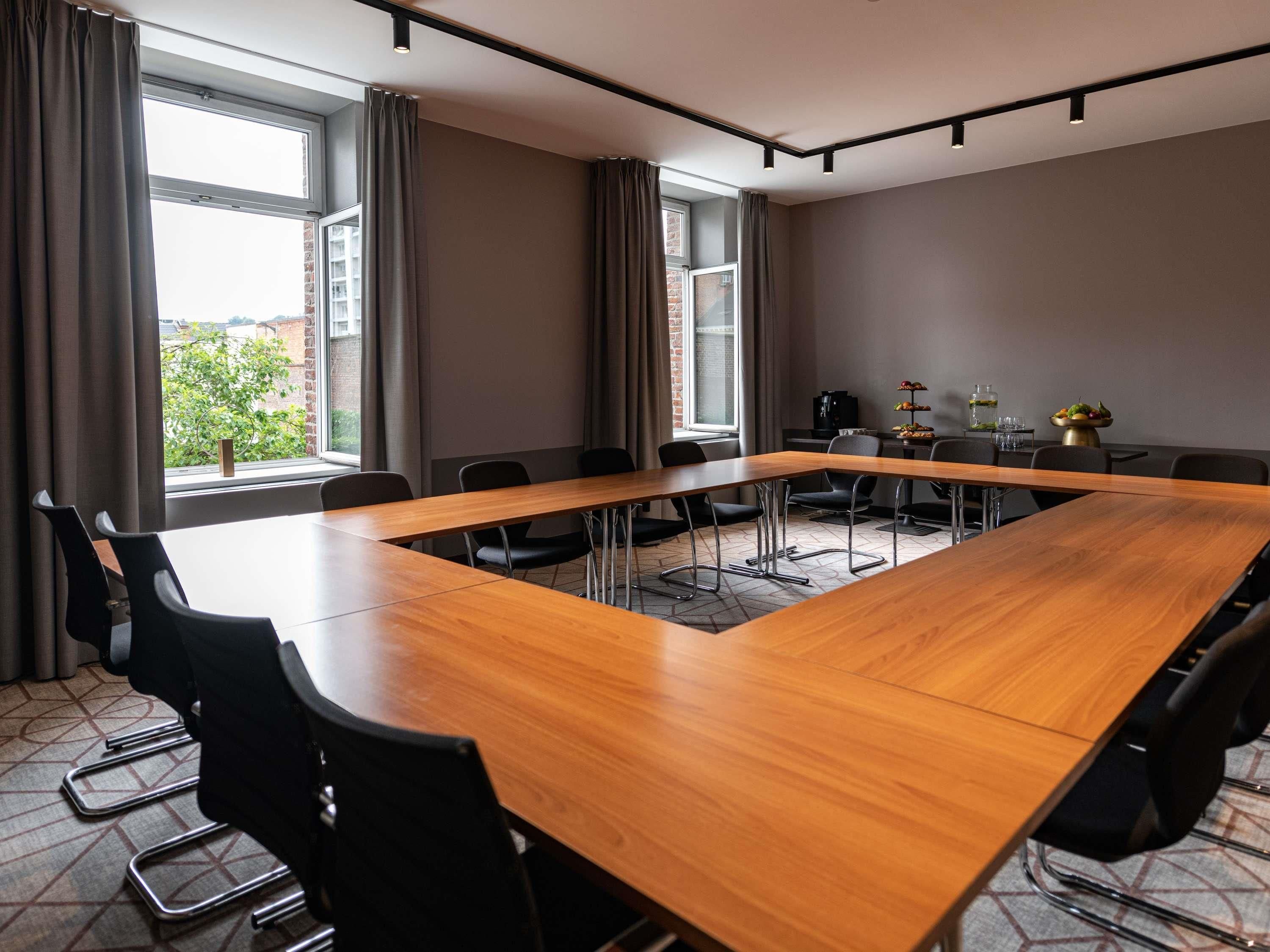 A conference room with a long wooden table, black chairs, and large windows with curtains.
