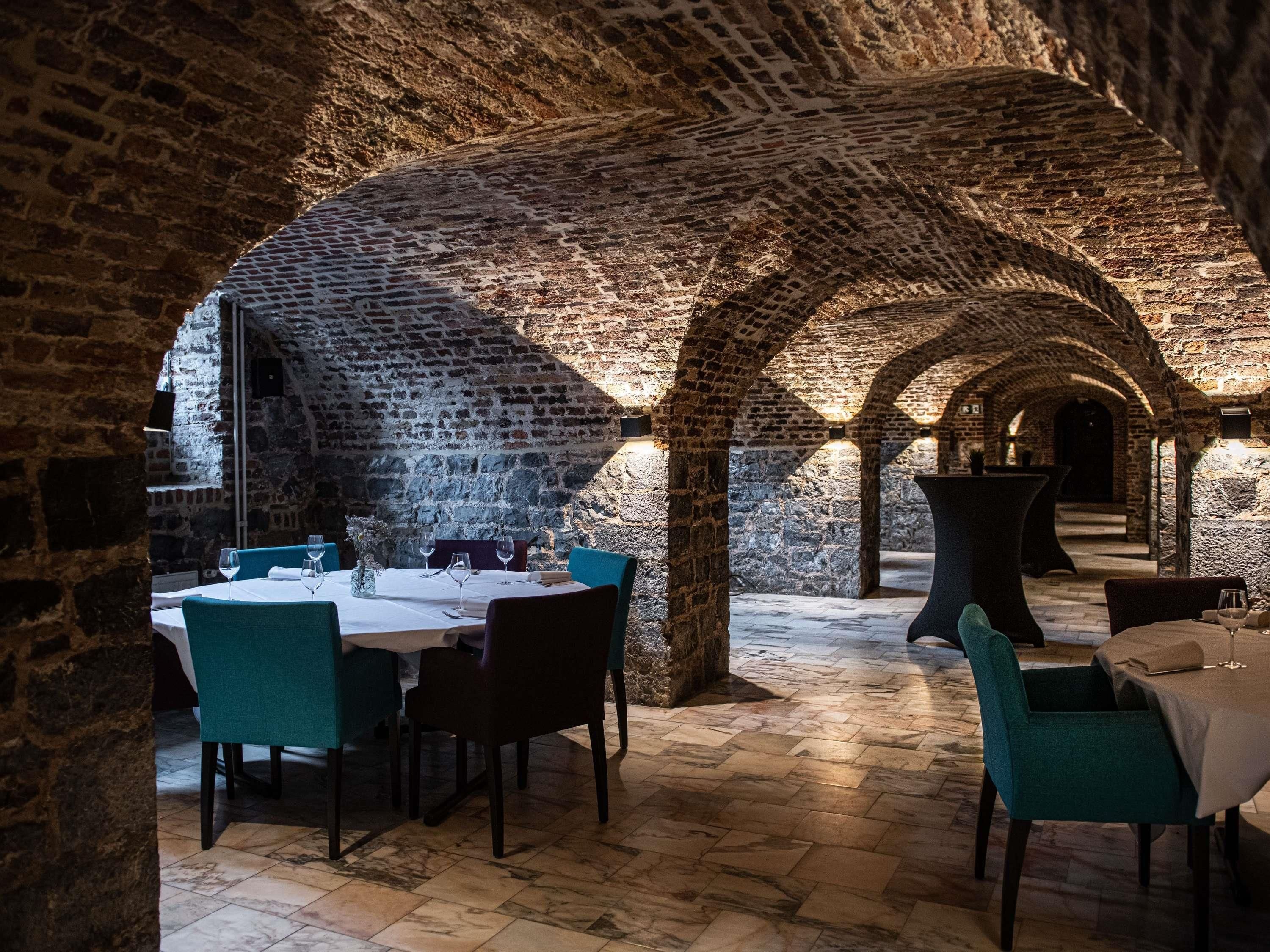 An underground dining area with brick arches, tables with chairs, and a stone floor.