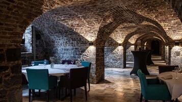 An underground dining area with brick arches, tables with chairs, and a stone floor.