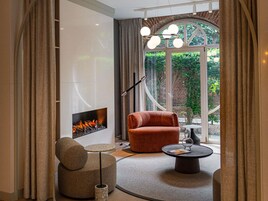 Una sala de estar moderna con chimenea, un sofá cómodo, una mesa de centro redonda y vistas a zonas verdes a través de amplios ventanales.