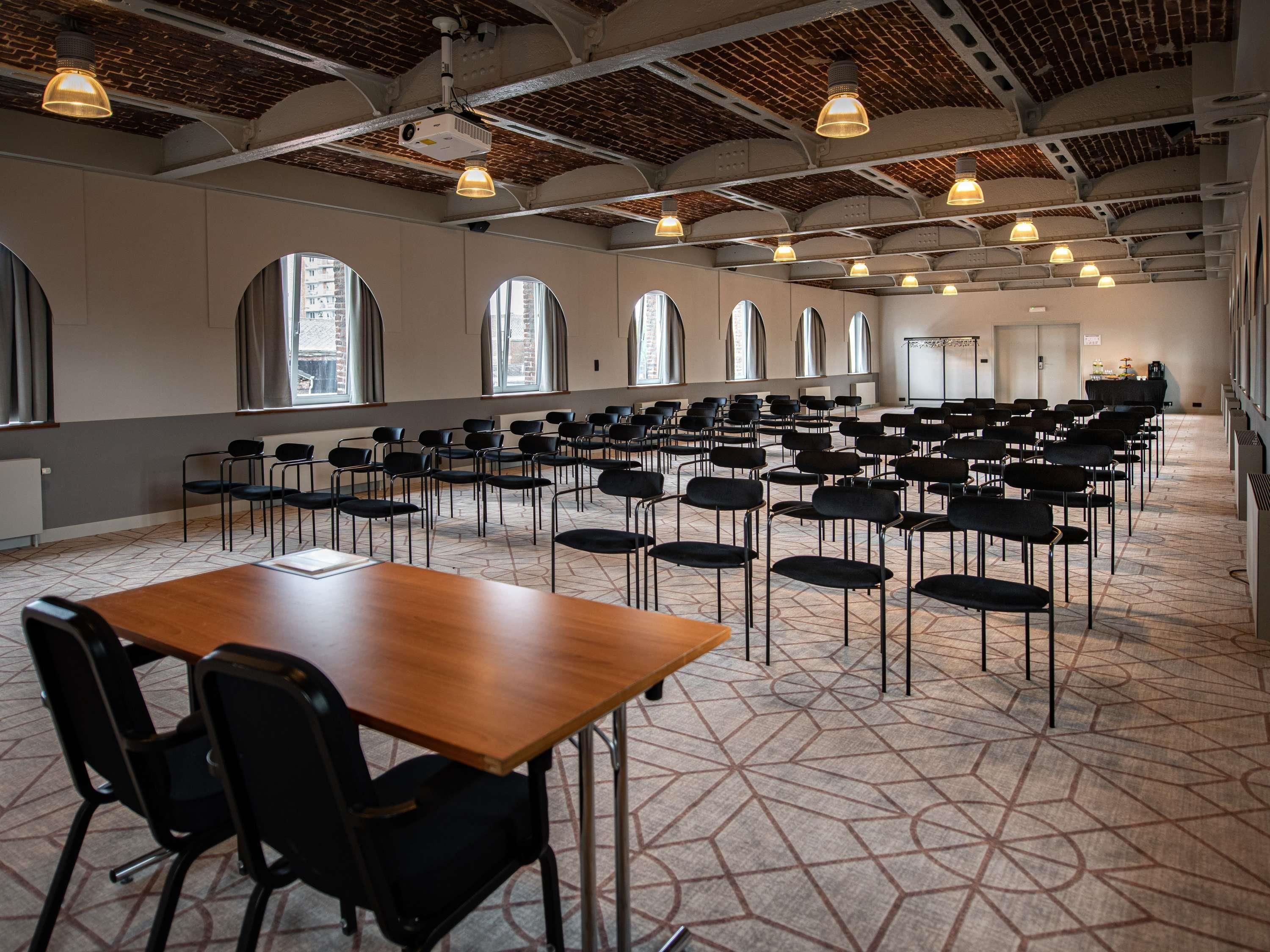 A conference room with a brick ceiling, large windows, and rows of black chairs.