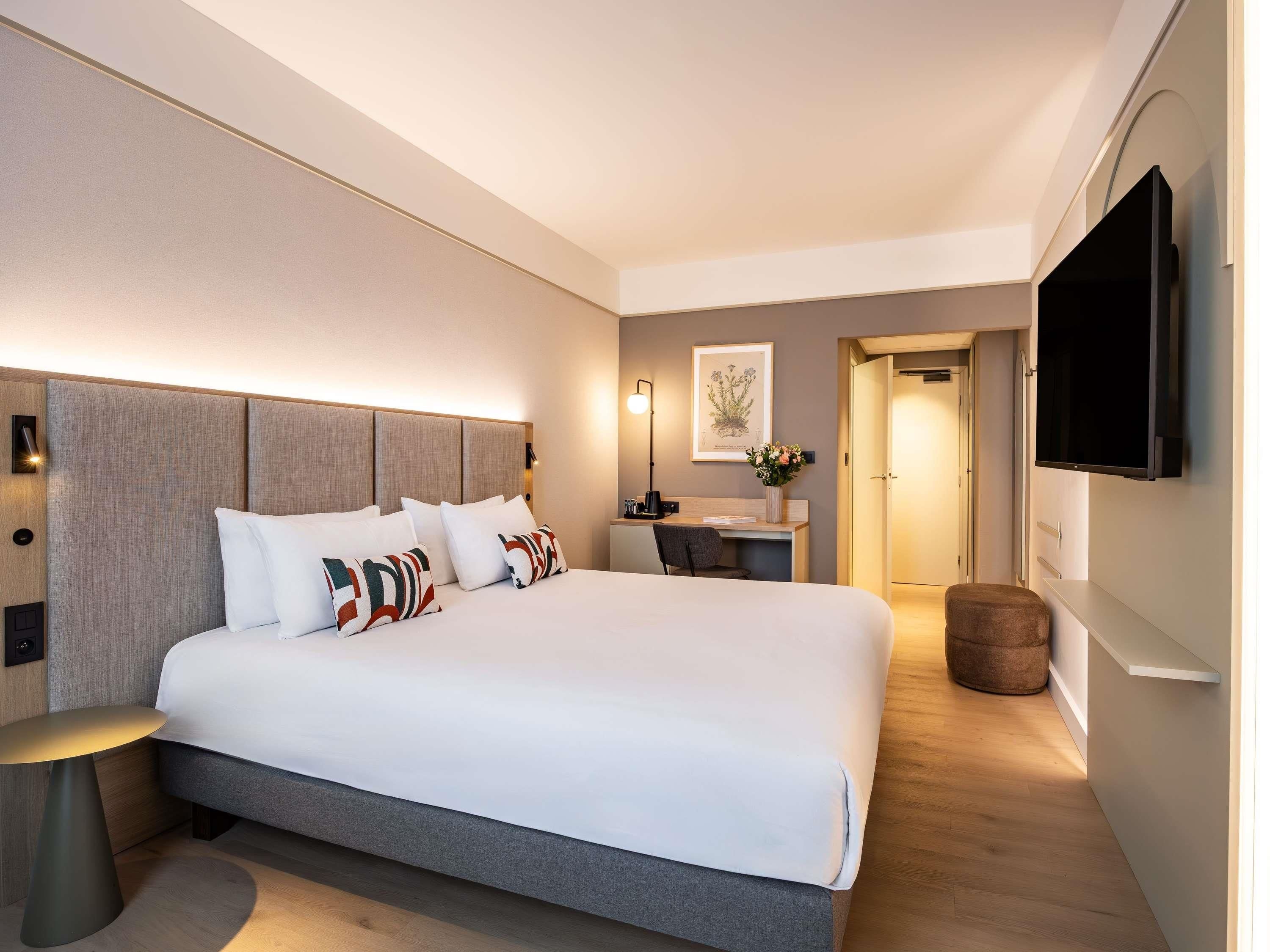 Una habitación de hotel moderna con una cama grande, mesitas de noche, un escritorio y un televisor de pantalla plana montado en la pared.