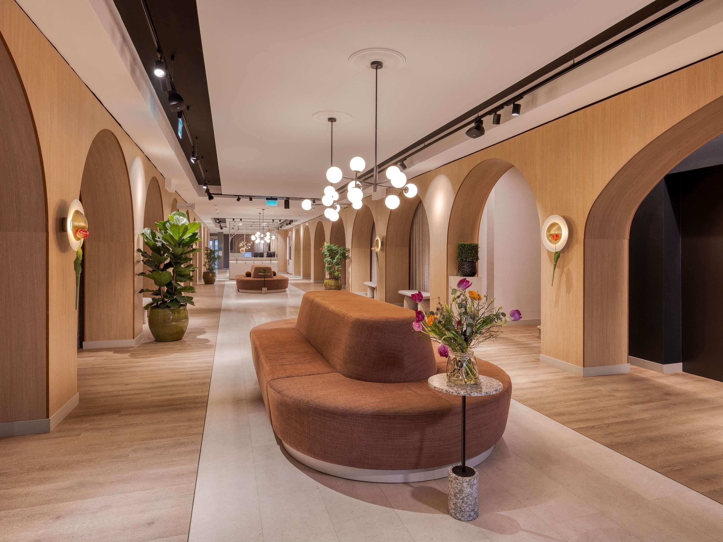 Een moderne hotel lobby met een centraal zitgedeelte, houten gewelfde wanden en een lange gang.