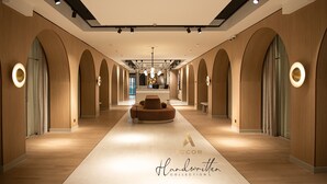 Un moderno vestíbulo de hotel con una zona de estar central, puertas en arco y un mostrador de recepción.